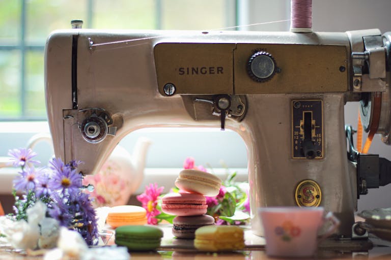 A classic sewing machine surrounded by flowers and colorful macarons, creating a nostalgic scene.