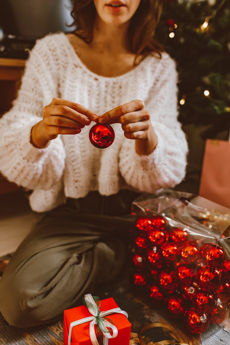 Woman decorating for Christmas with red baubles and a wrapped gift box.